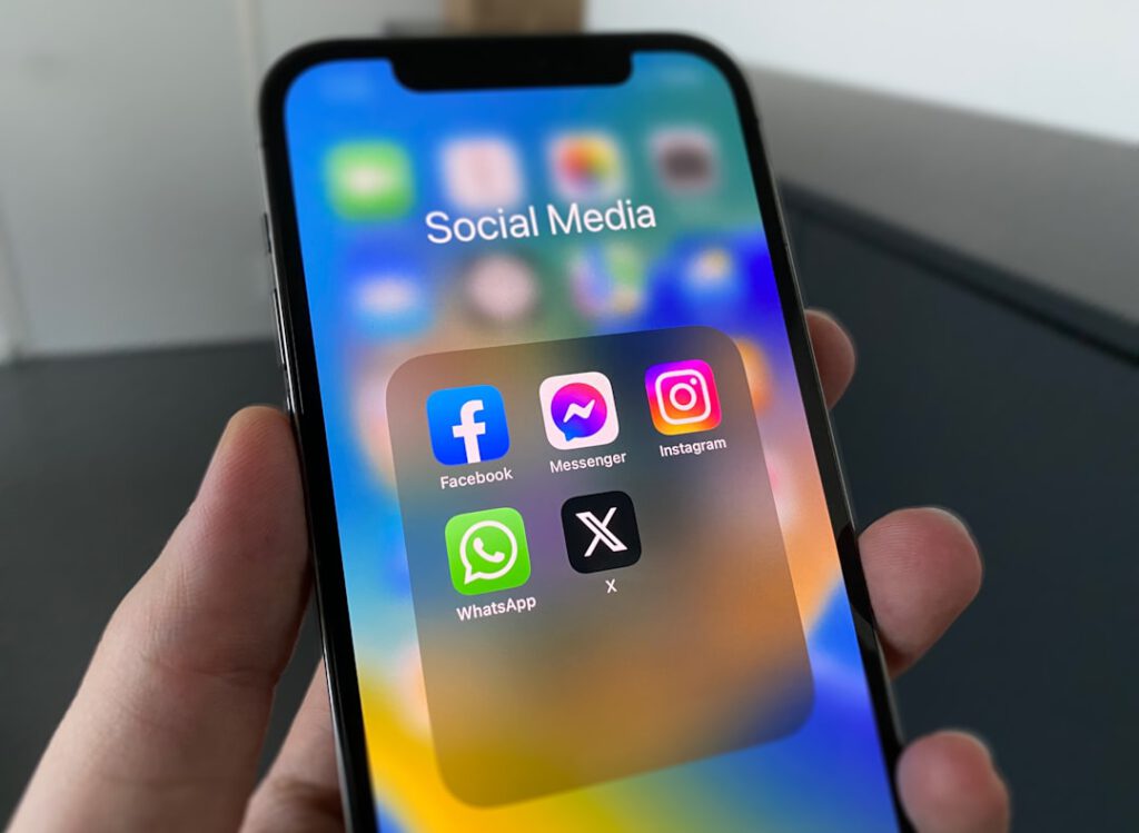 Mano sosteniendo un iPhone con apps de redes sociales, donde injurias online pueden ser delito según Bufete Paredes & Asociados