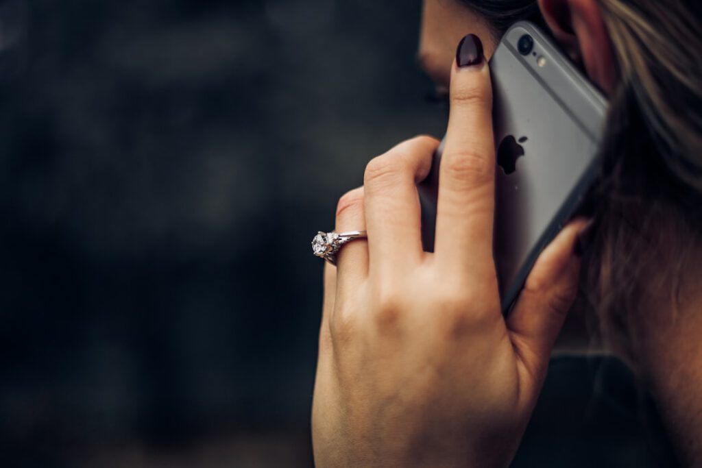 Mujer con anillo de compromiso hablando por iPhone tras vaciar su cuenta en una llamada del banco, caso para Bufete Paredes & Asociados