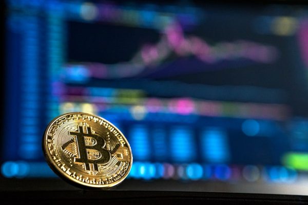 Moneda de Bitcoin ante gráficas de inversión, símbolo de estafas en plataformas cripto que Bufete Paredes & Asociados ayuda a recuperar